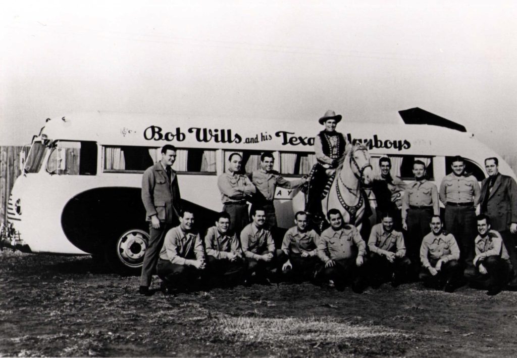 Bob Wills and his band, the Texas Playboys. The group poses in front of their tour bus, which is labeled "Bob Wills and His Texas Playboys."